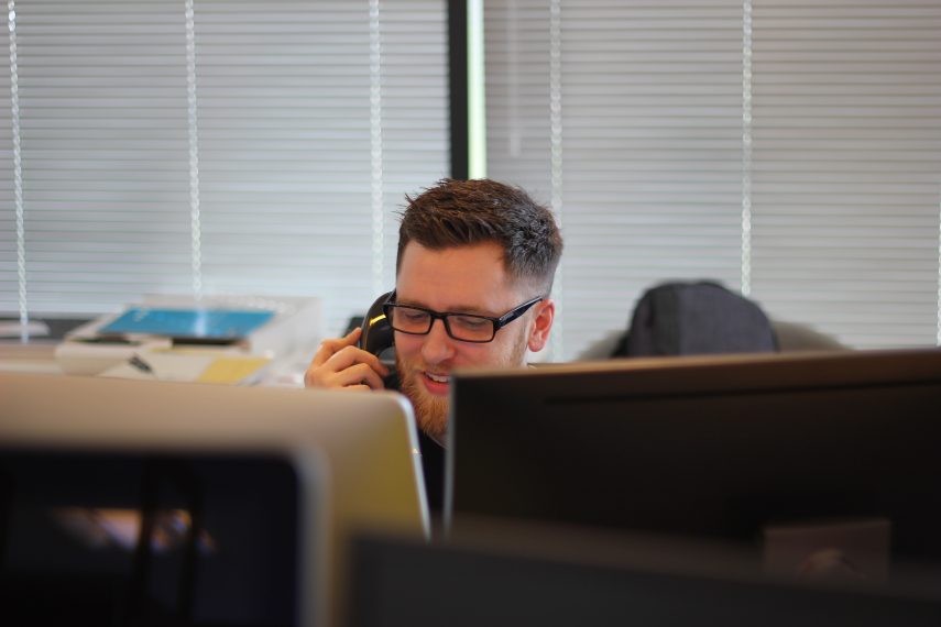 Person on phone while sitting in front of dual computer screens