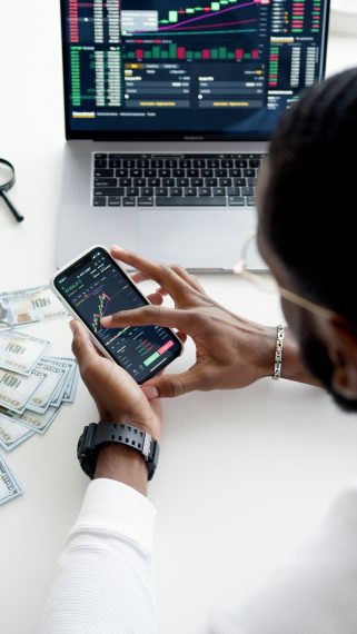 man using his phone to manage his money, with dollar bills and a laptop in the background