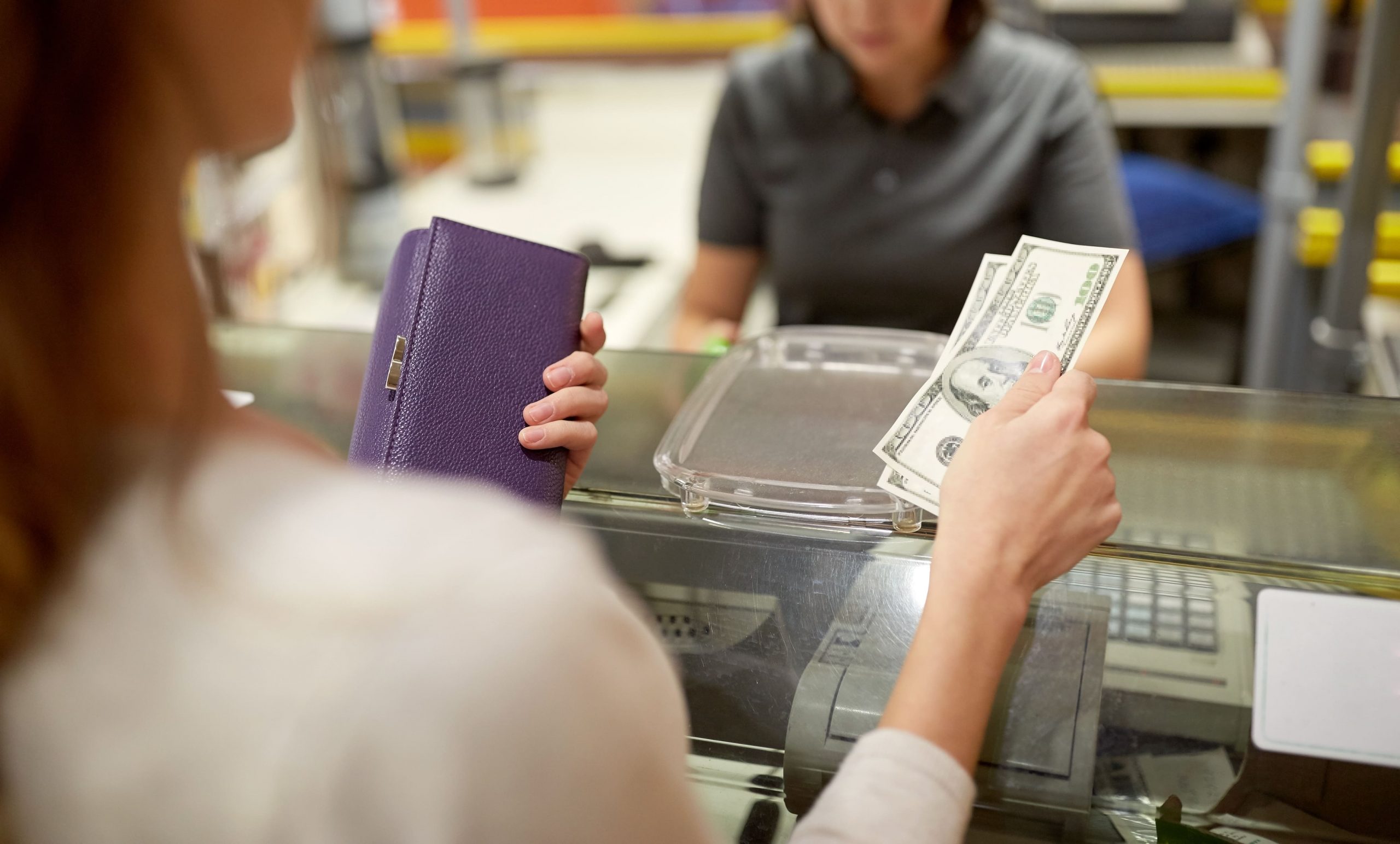 Photo of woman holding a purple wallet and paying cash at a register